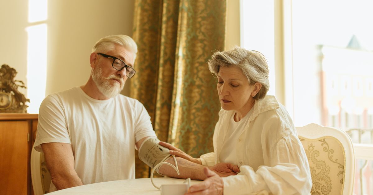 An elderly couple at home measuring blood pressure with a digital monitor, depicting care and health awareness.